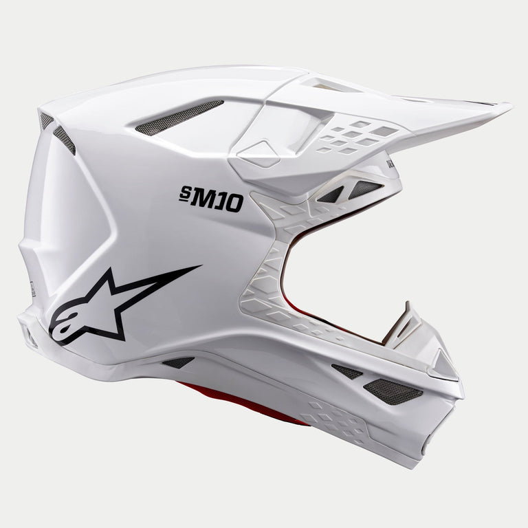 Casque Alpinestars Supertech M10 Solid, casque de motocross, blanc brillant, vue de profil montrant les logos S-M10 et Astars noirs, coque aérodynamique avec ouvertures de ventilation en maille, large visière blanche, protection avancée pour la course tout-terrain.