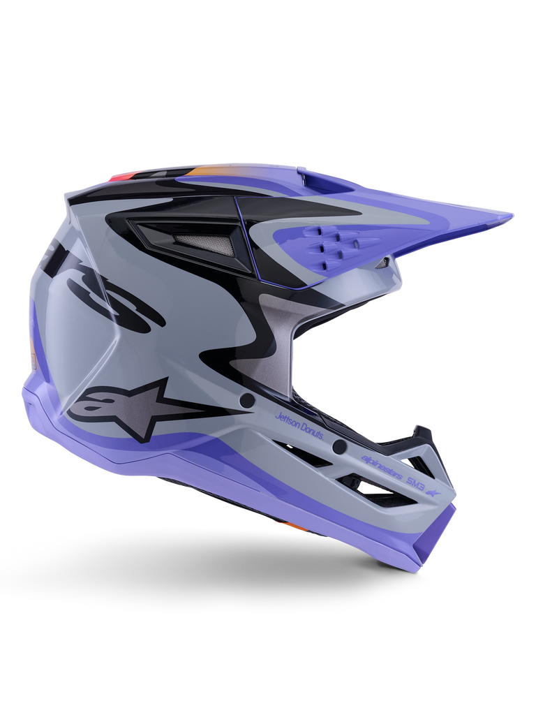 Casque Alpinestars S-M3 Jettson ECE 22.06, casque de motocross, gris, violet et noir brillant, vue de profil avec visière et mentonnière violettes, coque aérodynamique avec graphismes noirs, multiples aérations et marquage « Jettson Donuts » sur le côté.