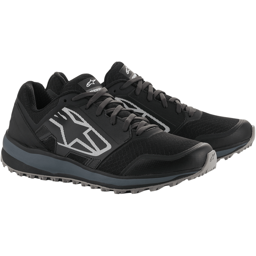 Chaussures Alpinestars Meta Trail, chaussures de course performantes, noir et gris foncé, grand logo Astars blanc rayé sur le côté, conception à lacets avec une semelle grise robuste, conçues pour un confort tout au long de la journée dans le paddock