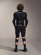 Veste de protection Alpinestars A-Impact Plasma - Manches longues, vue de dos, noire avec logos Alpinestars blancs, portée avec un short de protection et des genouillères pour une protection intégrale en VTT