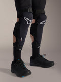 Genouillères Alpinestars A-Impact Plasma Pro, noir et blanc, avec le marquage de la technologie Nucleon PLASMA, portées avec des chaussettes noires et des chaussures de VTT noires, sangles à crochet et boucle sécurisées, équipement de protection ergonomique pour le cyclisme tout-terrain