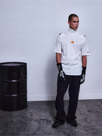 Alpinestars RSRV Pyro SS Tee, t-shirt blanc à col montant et manches courtes avec logo orange, porté avec gants noirs à motifs blancs, style streetwear premium