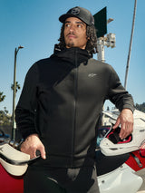Sweat à capuche Alpinestars Cypher, polaire lifestyle zippée noire, capuche à col haut avec logo, petit logo Astars blanc sur la poitrine, porté avec une casquette noire par un pilote tenant un casque de motocross blanc, style streetwear décontracté