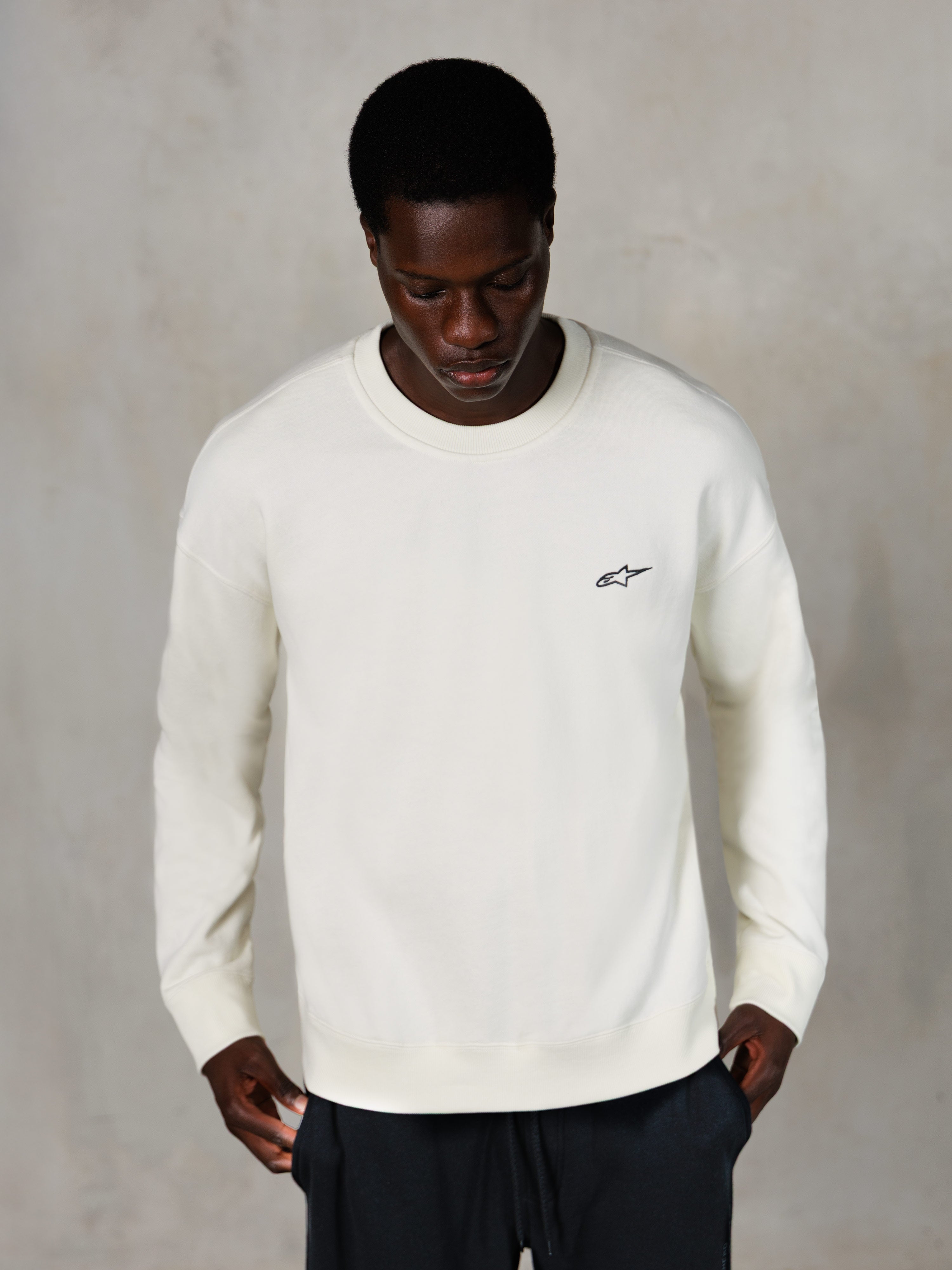 Alpinestars Essentials Ageless Crew, sweat-shirt à col rond, blanc cassé, petit logo Alpinestars noir sur la poitrine, porté par un mannequin, streetwear décontracté, polaire douce haut de gamme
