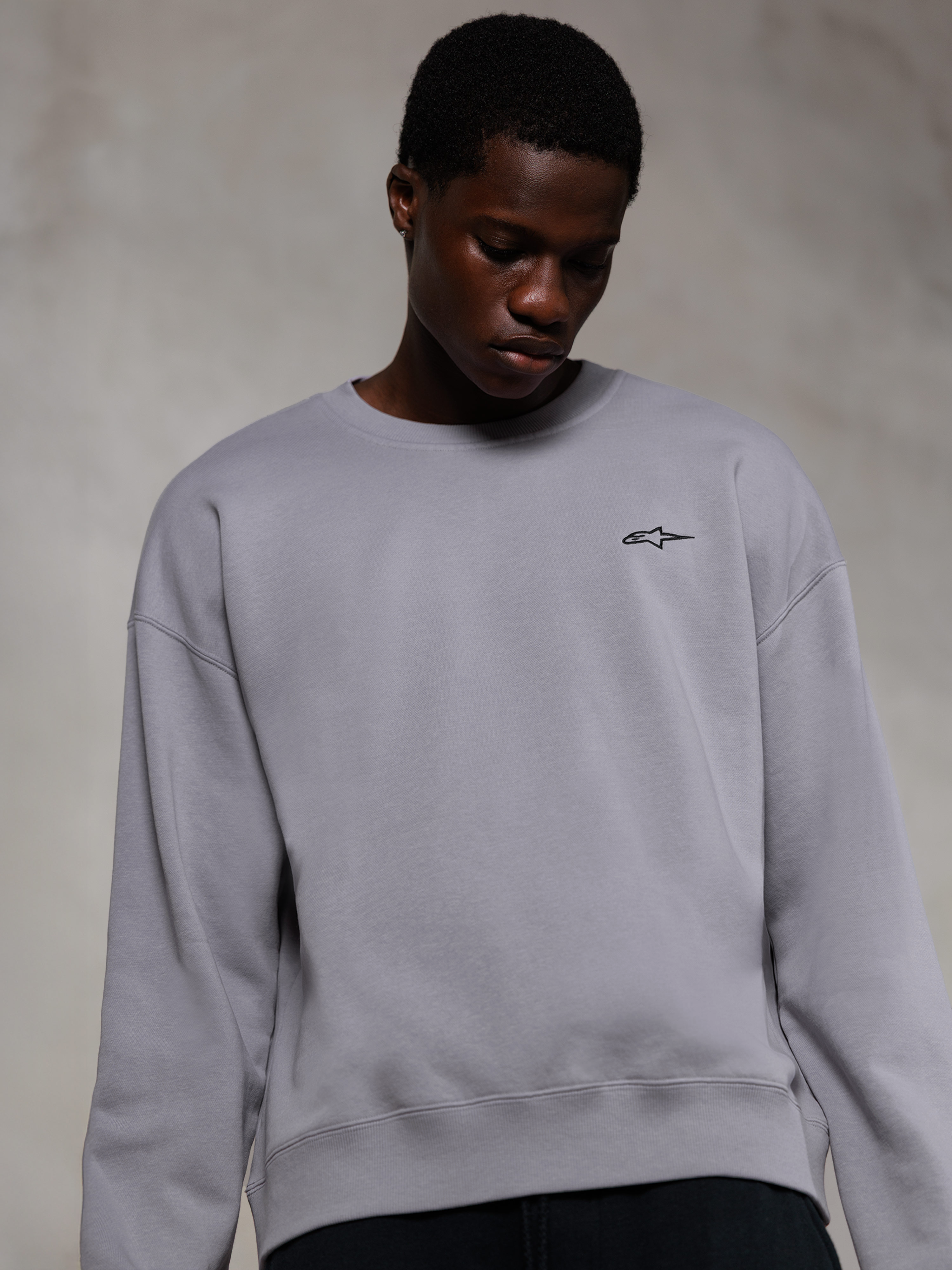 Alpinestars Essentials Ageless Crew, sweat-shirt à col rond premium argenté, avec un petit logo Alpinestars noir sur la poitrine, porté par un mannequin, style streetwear décontracté avec une texture polaire douce