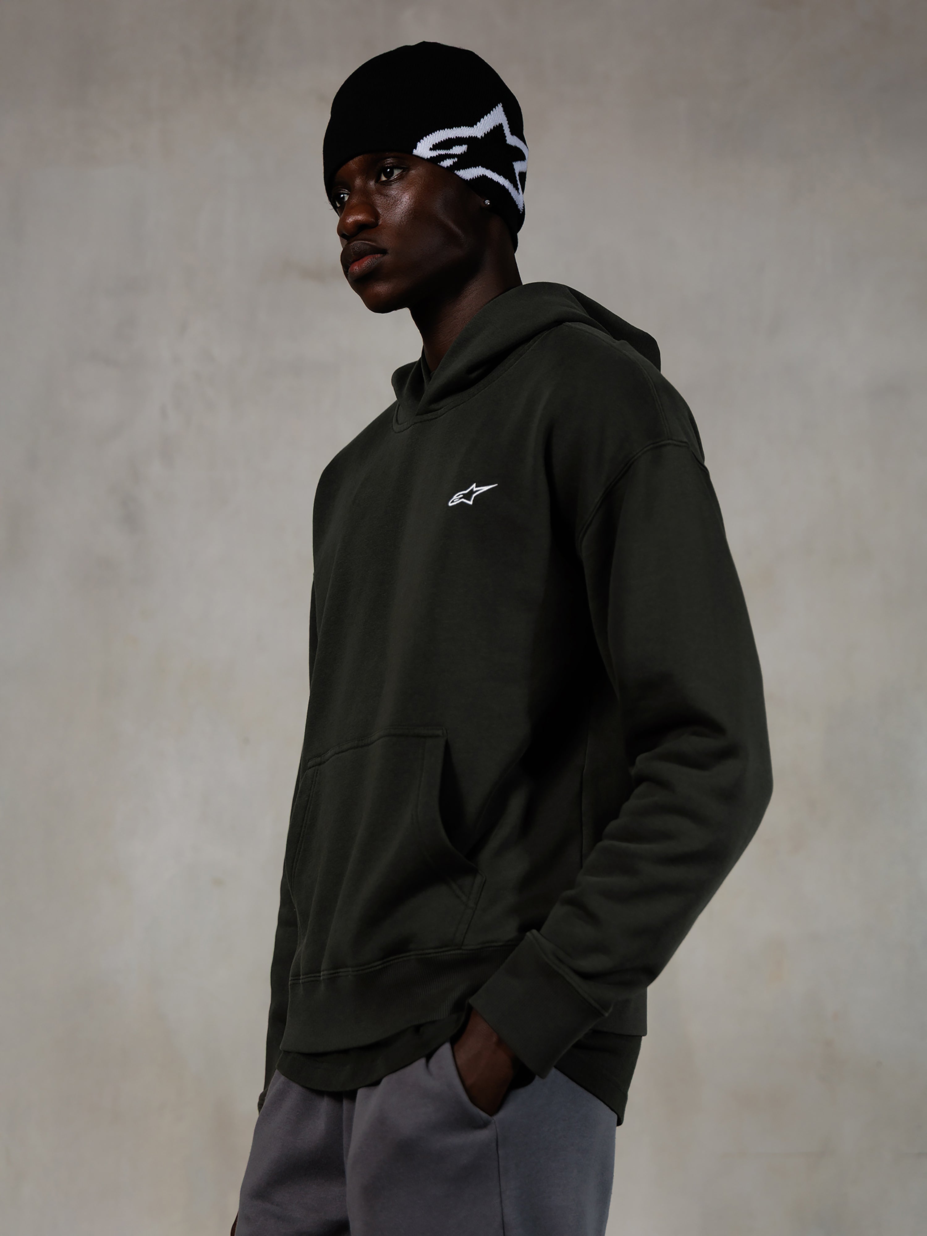 Sweat à capuche Alpinestars Essentials Ageless, Off Black, mannequin homme portant un style streetwear décontracté, molleton gris charbon délavé avec un petit logo étoile blanc, associé à un bonnet Alpinestars noir et un pantalon gris