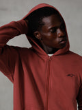 Sweat à capuche zippé Essentials Ageless Alpinestars, rouge brique, streetwear décontracté, capuche relevée avec la main derrière la tête, petit logo Astars noir sur la poitrine, sweat en polaire à coupe décontractée