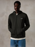 Sweat à capuche zippé Alpinestars Essentials Ageless, Off Black, sweat à capuche entièrement zippé avec un petit logo Alpinestars blanc sur la poitrine, coupe décontractée, porté par un mannequin avec un jean bleu et un t-shirt blanc, style streetwear décontracté inspiré du sport automobile