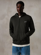 Sweat à capuche zippé Alpinestars Essentials Ageless, Off Black, sweat à capuche entièrement zippé avec un petit logo Alpinestars blanc sur la poitrine, coupe décontractée, porté par un mannequin avec un jean bleu et un t-shirt blanc, style streetwear décontracté inspiré du sport automobile