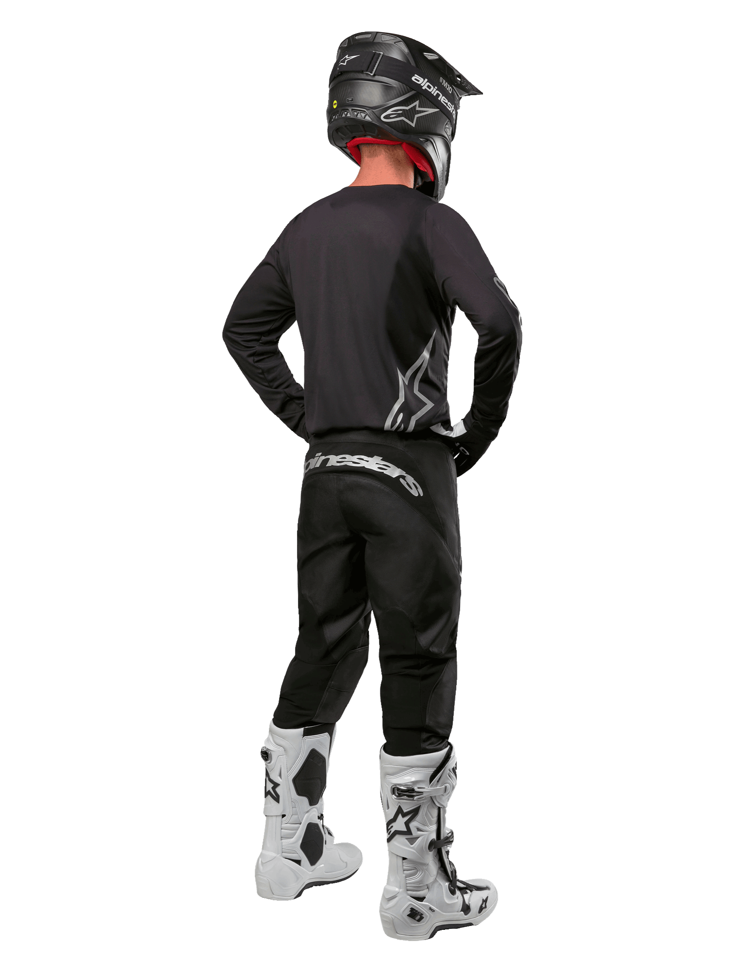 Ensemble d'équipement Alpinestars 2024 Fluid Graphite, pilote de motocross vu de dos, maillot et pantalon gris graphite avec logos Alpinestars argentés, casque noir et bottes de motocross blanches, tenue à coupe athlétique pour la conduite tout-terrain