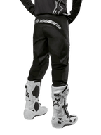 Pantalon Alpinestars Fluid Graphite 2024, pantalon de motocross, noir et argent, vue arrière montrant le marquage Alpinestars argenté sur l'empiècement arrière, porté avec des bottes de motocross blanches et noires, conception en textile durable pour le tout-terrain
