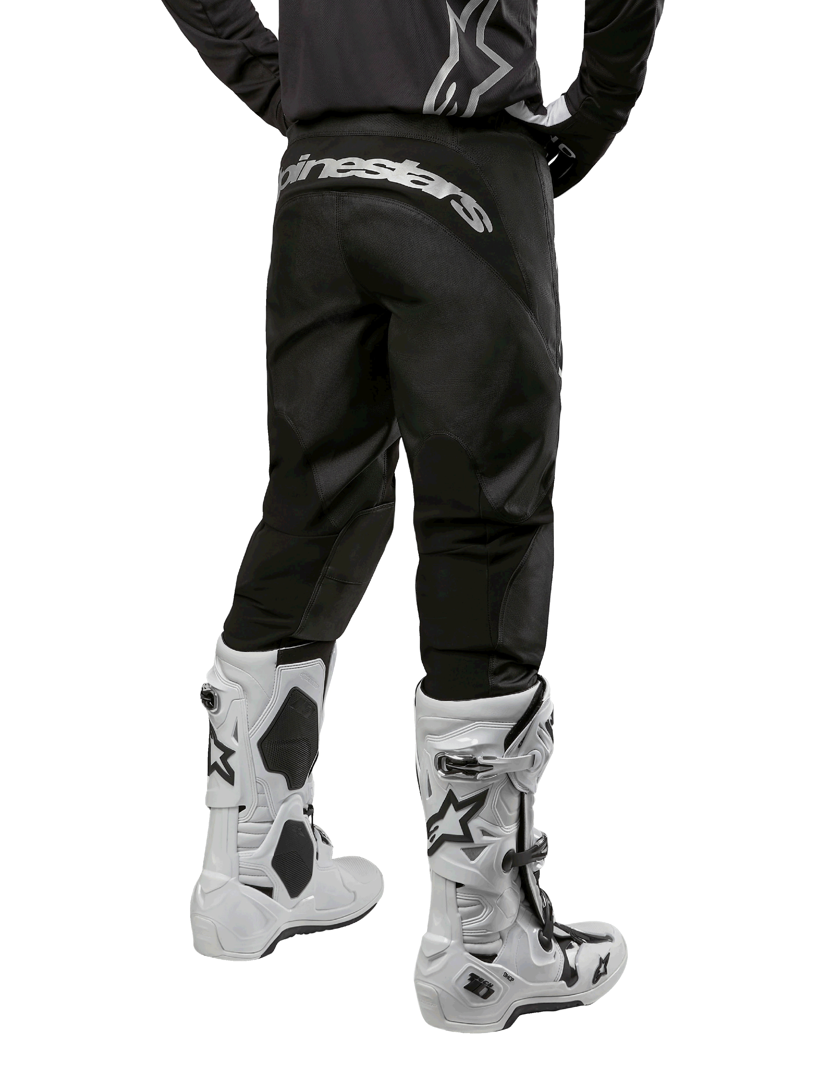 Pantalon Alpinestars Fluid Graphite 2024, pantalon de motocross, noir et argent, vue arrière montrant le marquage Alpinestars argenté sur l'empiècement arrière, porté avec des bottes de motocross blanches et noires, conception en textile durable pour le tout-terrain
