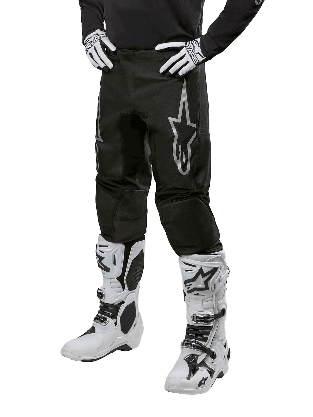 Alpinestars 2024 Fluid Graphite Pants, pantalon de motocross, noir et argent, avec un logo Alpinestars argenté sur la cuisse, présenté porté avec des bottes et des gants de motocross blancs, conçu pour la course de moto tout-terrain