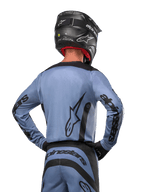 Maillot Alpinestars 2024 Fluid Lurv, maillot de motocross, bleu clair et noir, vue arrière du pilote montrant le grand logo étoilé et le marquage sur les manches, porté avec un casque noir et un pantalon tout-terrain assorti, équipement de course professionnel