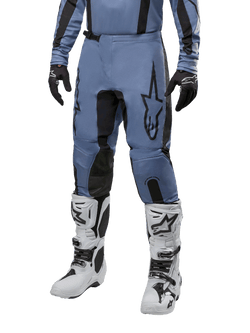 Pantalon Alpinestars Fluid Lurv 2024, pantalon de motocross, bleu clair et noir, porté avec un maillot à manches longues assorti et des bottes de motocross blanches, doté d'un logo étoile noire sur la cuisse et de panneaux intérieurs de genoux renforcés, vue de face sur fond blanc