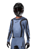 Pilote de motocross portant le maillot Alpinestars 2024 Fluid Lurv, bleu clair et noir, associé à un casque et des lunettes noirs, avec des motifs graphiques noirs et le logo étoile Alpinestars, équipement de performance athlétique pour la course tout-terrain.