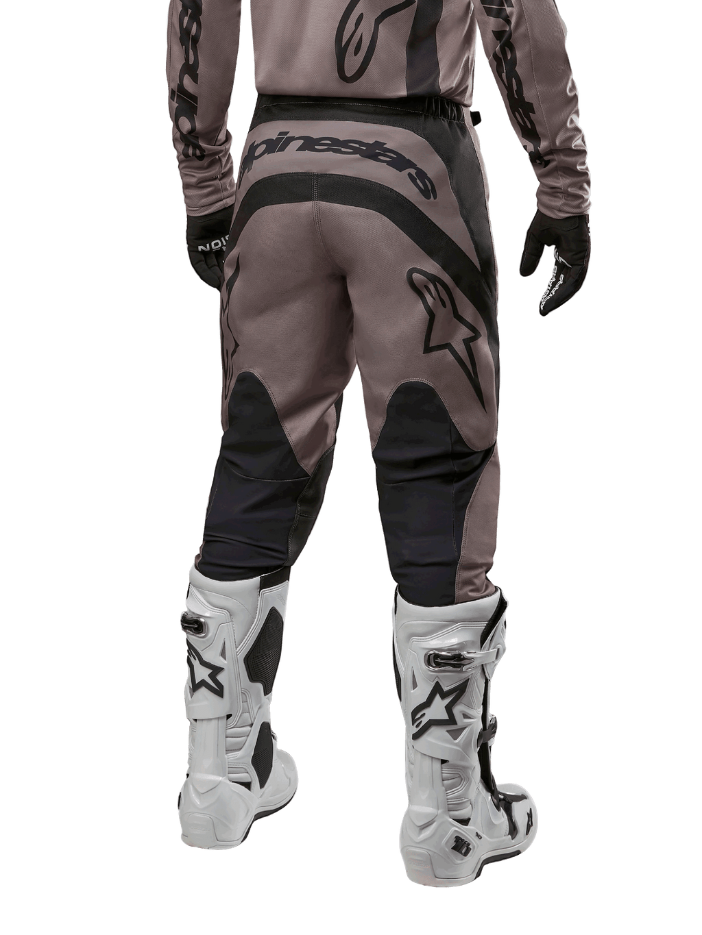 Alpinestars Fluid Lurv Pants 2024, pantalon de motocross, Mud Black, vue arrière montrant un large logo Alpinestars noir sur l'assise et des empiècements noirs aux mollets, porté avec des bottes de motocross noires et blanches et un maillot assorti.