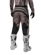 Alpinestars Fluid Lurv Pants 2024, pantalon de motocross, Mud Black, vue arrière montrant un large logo Alpinestars noir sur l'assise et des empiècements noirs aux mollets, porté avec des bottes de motocross noires et blanches et un maillot assorti.