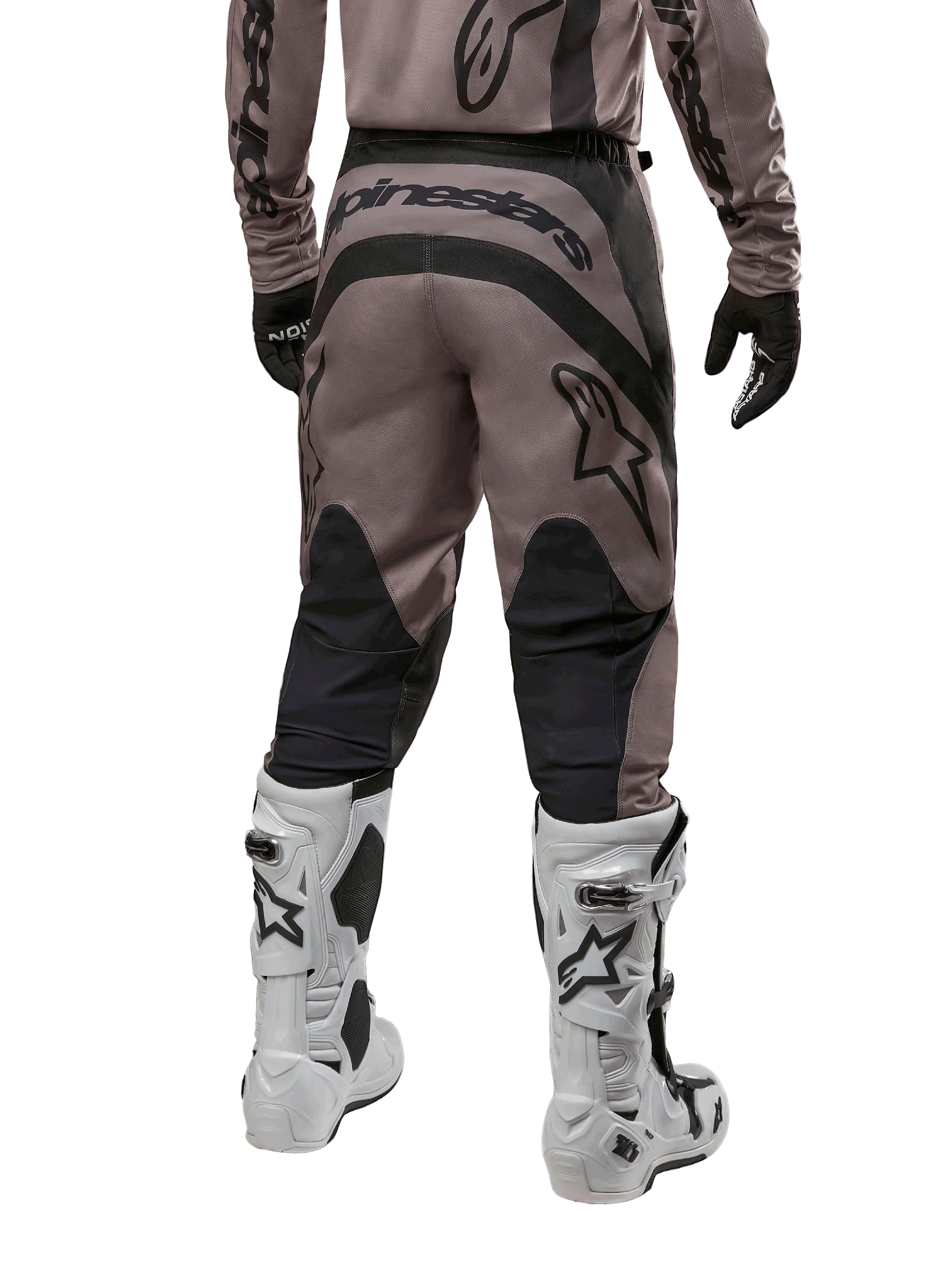 Alpinestars Fluid Lurv Pants 2024, pantalon de motocross, Mud Black, vue arrière montrant un large logo Alpinestars noir sur l'assise et des empiècements noirs aux mollets, porté avec des bottes de motocross noires et blanches et un maillot assorti.