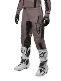 Alpinestars 2024 Fluid Lurv Pants, pantalon de motocross, Mud Black et noir, avec logo Alpinestars, porté avec gants noirs et bottes de motocross blanches, design sportif pour la course tout-terrain