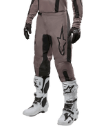 Alpinestars 2024 Fluid Lurv Pants, pantalon de motocross, Mud Black et noir, avec logo Alpinestars, porté avec gants noirs et bottes de motocross blanches, design sportif pour la course tout-terrain