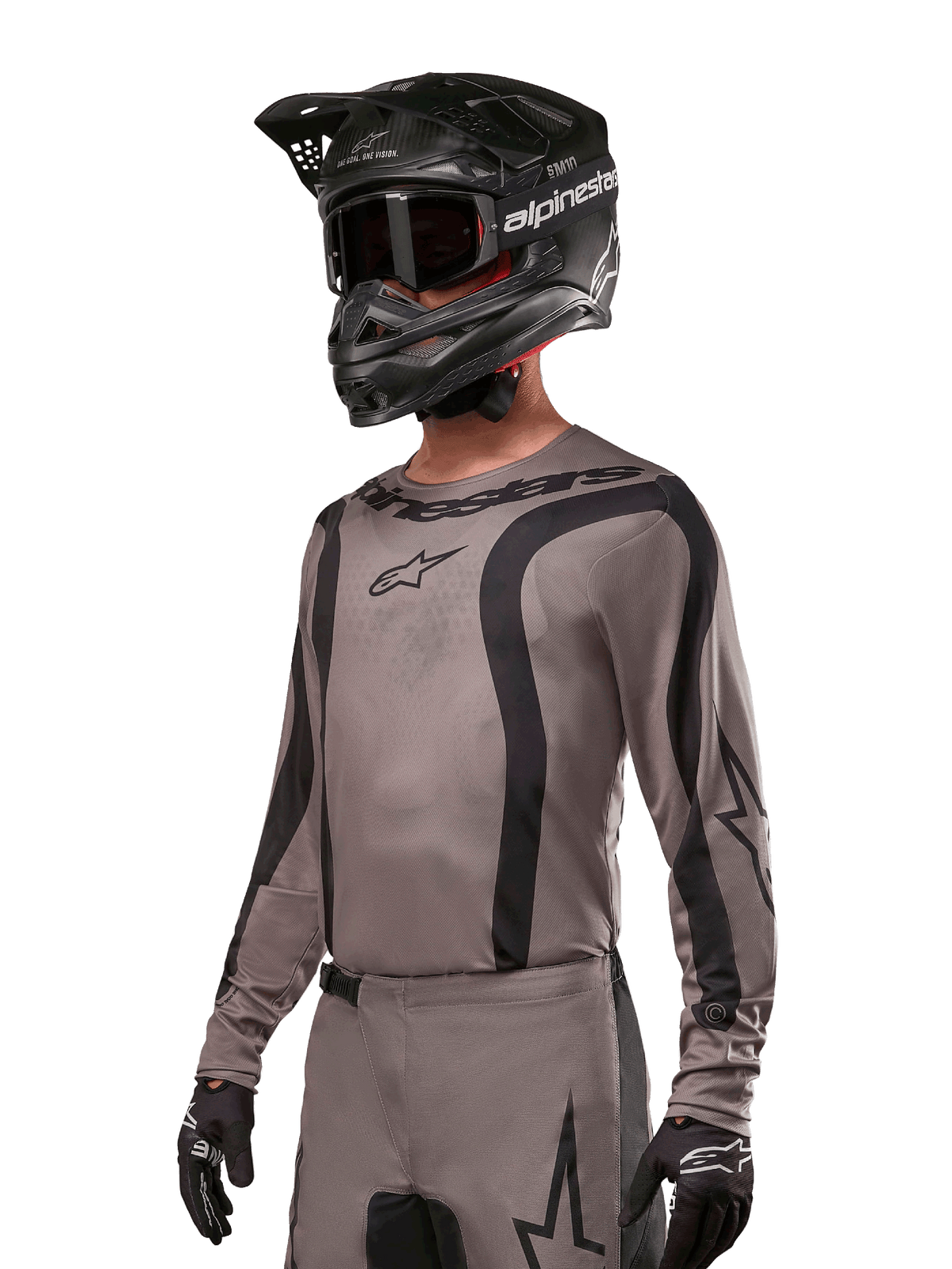 Maillot Alpinestars 2024 Fluid Lurv, maillot de motocross, gris et noir, design à manches longues avec rayures noires incurvées et logos, porté avec un pantalon assorti et un casque de motocross noir, équipement de course tout-terrain coordonné