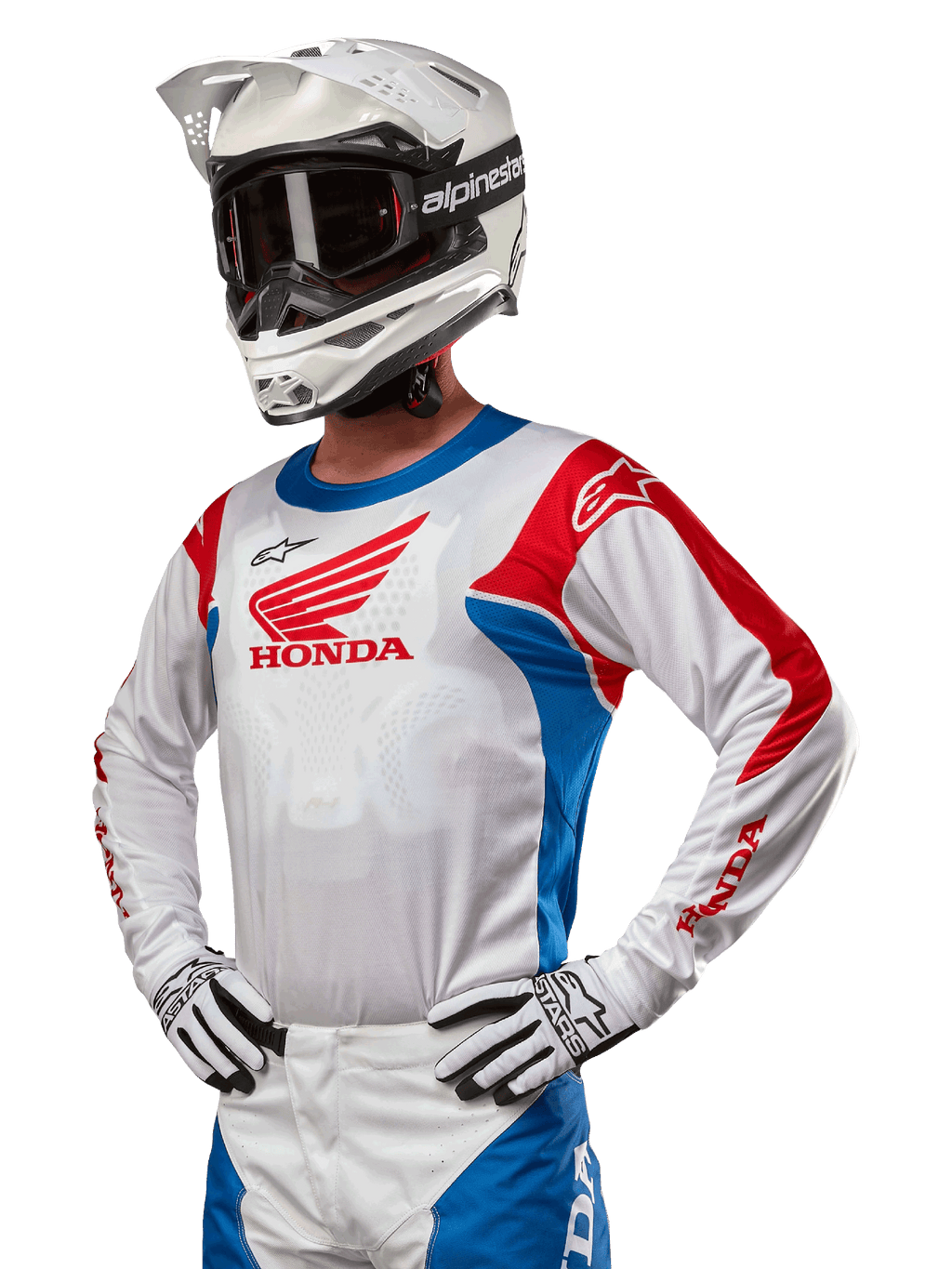 Pilote de motocross portant le maillot Honda Racer Iconic en blanc, bleu vif et rouge vif, avec un grand logo d'aile Honda sur la poitrine, associé à un casque Alpinestars blanc et des gants blancs et noirs assortis, équipement coordonné pour la performance tout-terrain