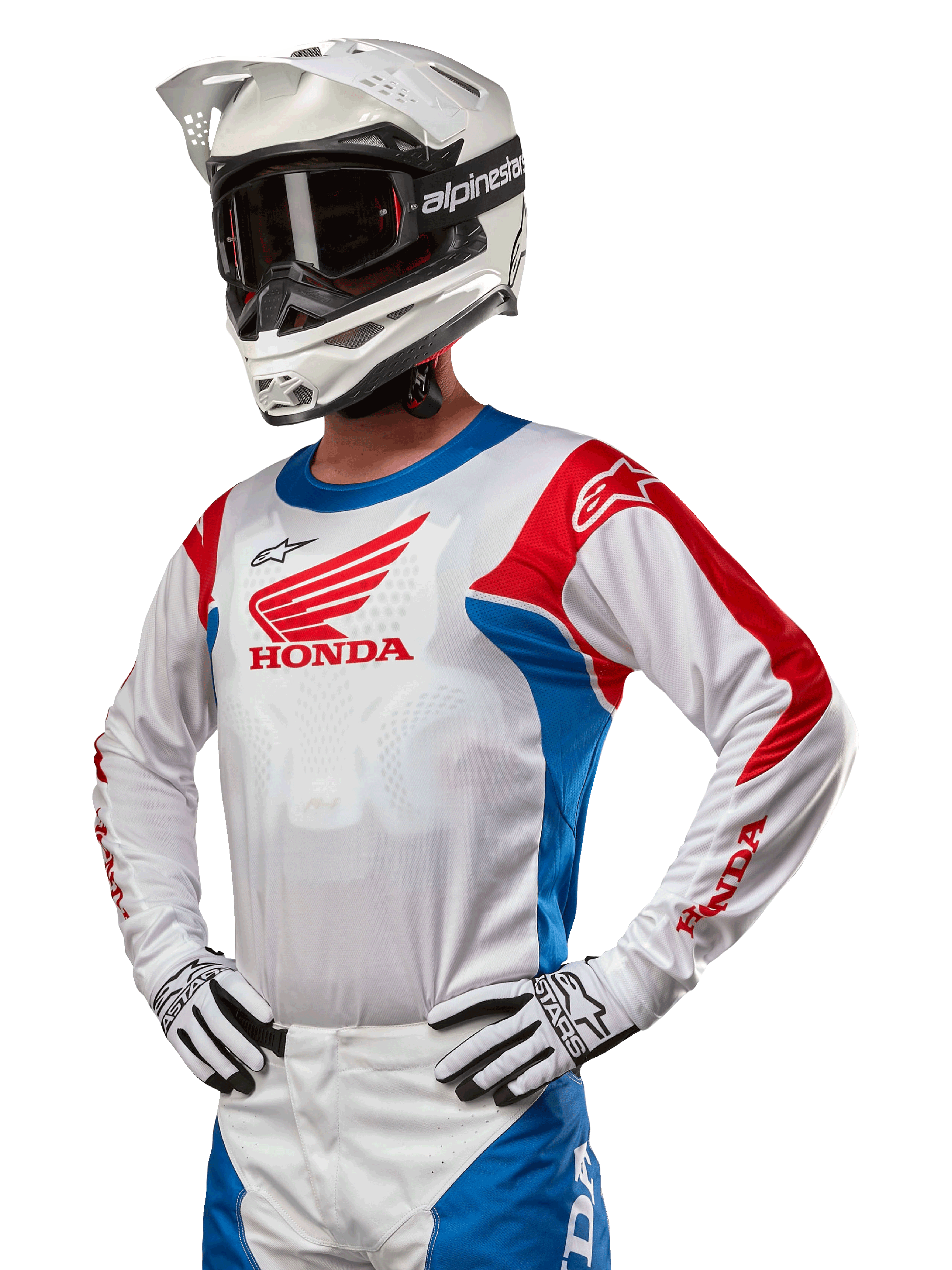 Pilote de motocross portant le maillot Honda Racer Iconic en blanc, bleu vif et rouge vif, avec un grand logo d'aile Honda sur la poitrine, associé à un casque Alpinestars blanc et des gants blancs et noirs assortis, équipement coordonné pour la performance tout-terrain