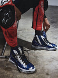 Alpinestars RSRV Legacy Shoe, baskets montantes bleues et blanches avec lacets noirs, portées avec pantalon de protection rouge et noir, design streetwear inspiré du sport automobile