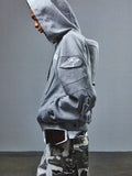 Alpinestars RSRV GP Hoodie, sweat à capuche gris avec logo étoile sur la manche, style décontracté sportif, porté avec pantalon camouflage et lunettes de protection