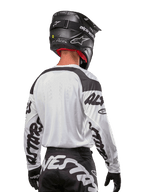 Maillot Alpinestars Racer Hana 2024, blanc et noir, vue de dos montrant la coupe ergonomique et le marquage imposant sur les manches, associé à un casque de motocross noir et un pantalon noir et blanc assorti, équipement de course haute performance pour la conduite tout-terrain