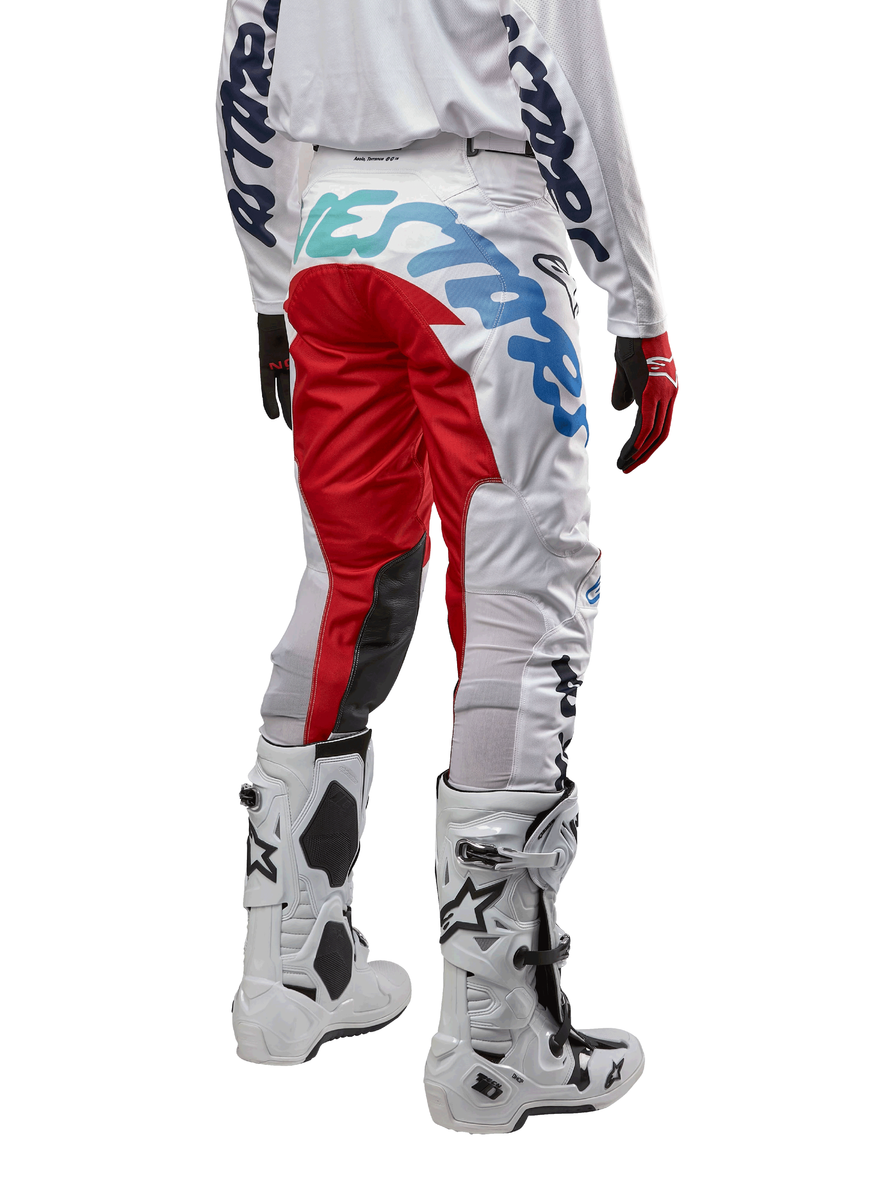 Alpinestars Racer Hana Pants 2024, pantalon de motocross, blanc multicolore avec des accents rouges et bleus, vue arrière montrant un marquage important sur l'assise, porté avec des bottes de motocross blanches et noires, conçu pour la performance et la durabilité en tout-terrain