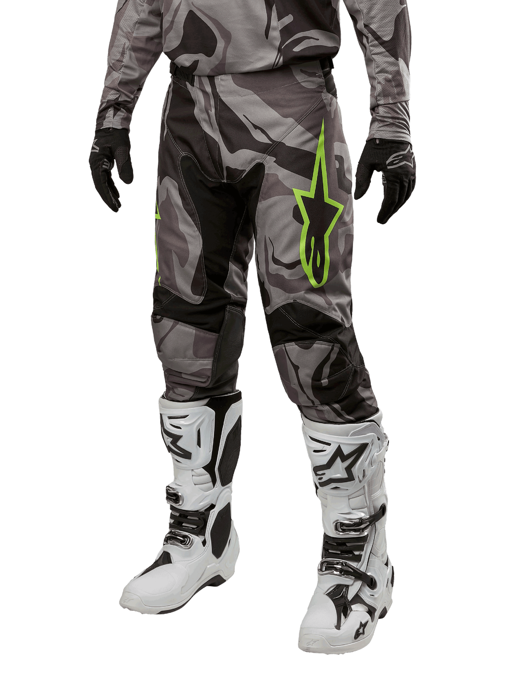 Alpinestars 2024 Racer Tactical Pants, pantalon de motocross, camouflage gris et noir, logo étoile vert citron, porté avec des bottes blanches et noires et des gants noirs, équipement de pilotage tout-terrain