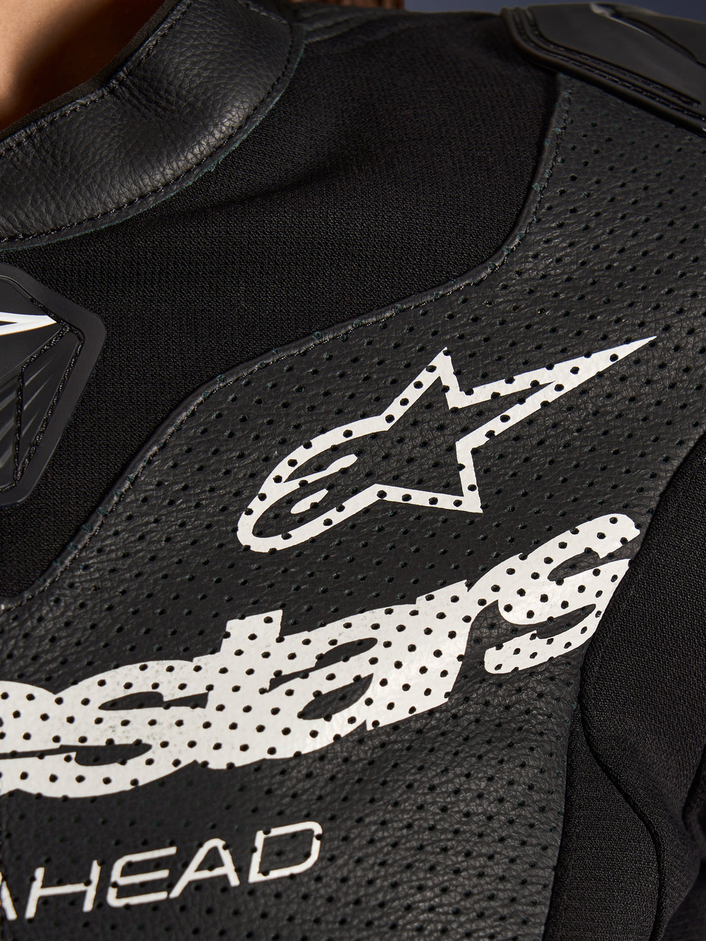 Gros plan sur la combinaison en cuir 2 pièces Alpinestars Stella GP-R7 en noir, avec des panneaux en cuir perforé, un grand logo Alpinestars blanc sur la poitrine et des sections en tissu extensible respirant.