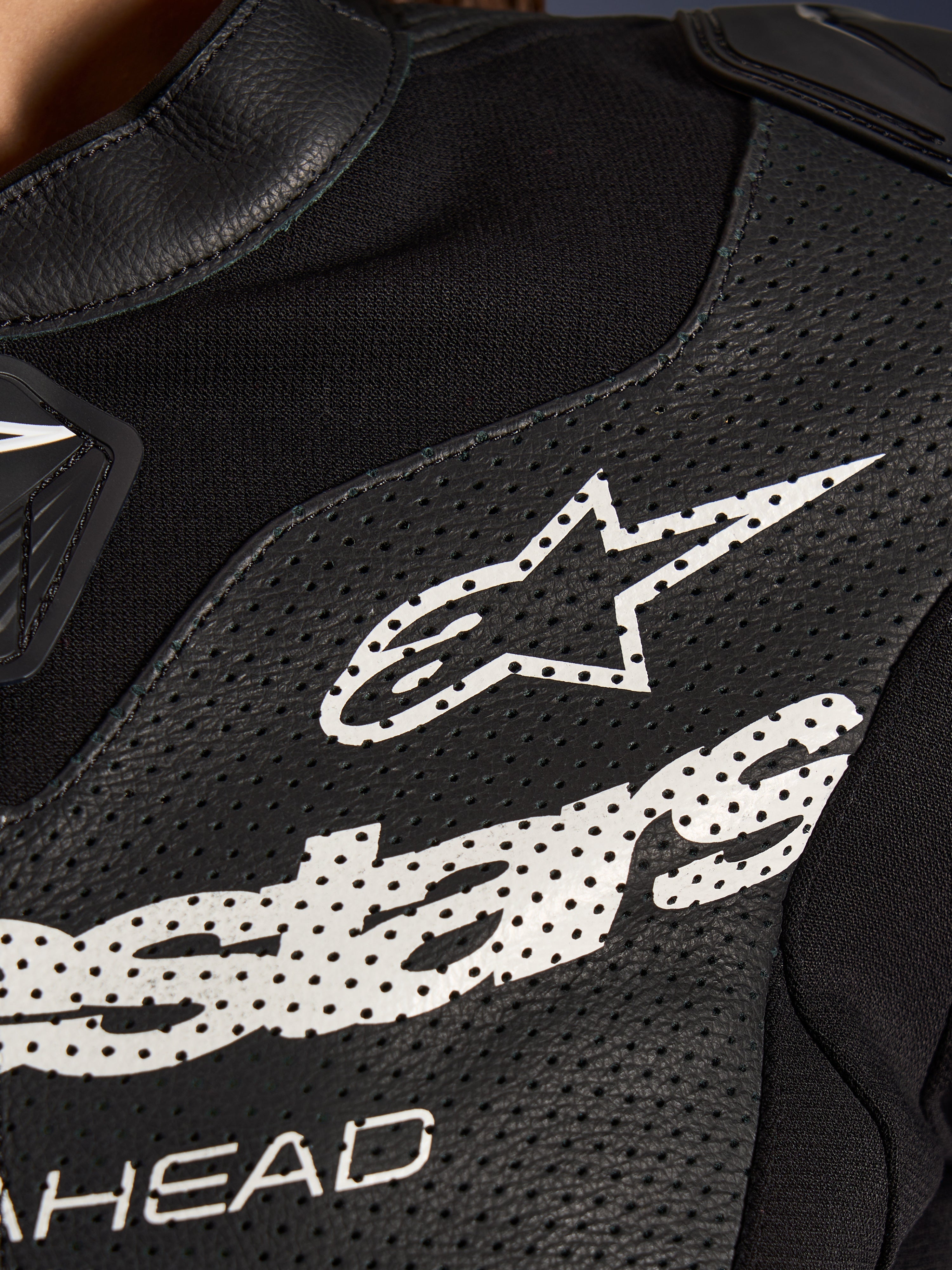 Gros plan sur la combinaison en cuir 2 pièces Alpinestars Stella GP-R7 en noir, avec des panneaux en cuir perforé, un grand logo Alpinestars blanc sur la poitrine et des sections en tissu extensible respirant.