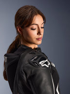 Femme portant la combinaison en cuir 2 pièces Alpinestars Stella GP-R7, vue rapprochée de l'épaule en cuir noir avec protection DFS RR et logo étoile blanc, présentant la bosse aérodynamique intégrée et les détails perforés.