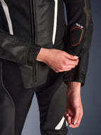 Gros plan sur la combinaison en cuir 2 pièces Alpinestars Stella GP-R7 en noir, mettant l'accent sur le réglage de la fermeture éclair de l'avant-bras, avec une construction en cuir perforé, des accents blancs et le marquage compatible Tech-Air sur la manche.