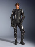 Femme portant la combinaison en cuir 2 pièces Alpinestars Stella GP-R7 en noir avec accents blancs, dotée de panneaux en cuir perforé et de logos blancs sur le torse et les genoux, assortie de gants et de bottes de course noirs, équipement professionnel de course de moto