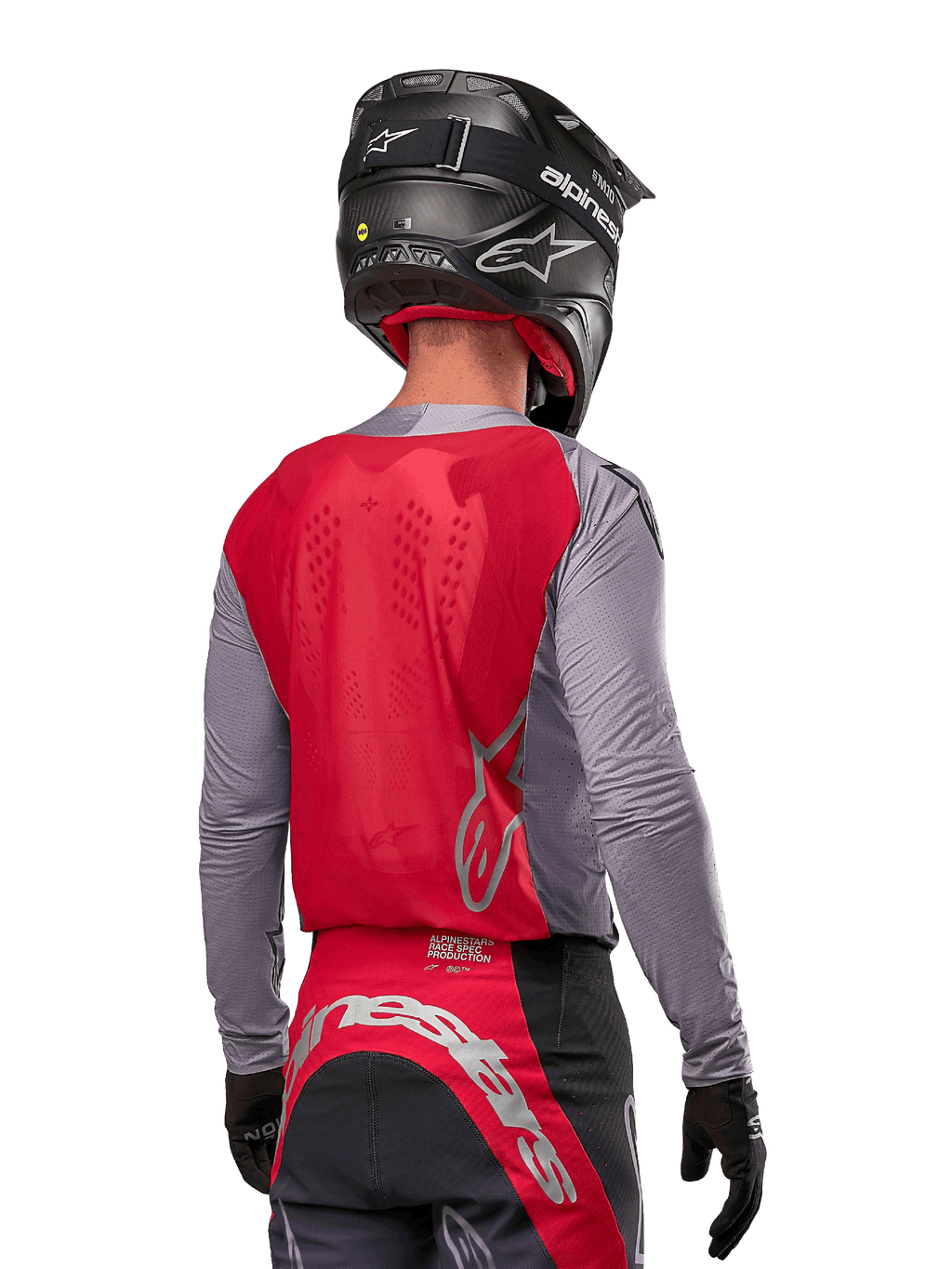 Pilote de motocross de dos portant le maillot Alpinestars 2024 Supertech Dade en Iron Red Berry et gris, doté d'un panneau arrière en mesh respirant et de logos argentés, associé à un casque noir et un pantalon de course assorti pour une performance tout-terrain professionnelle.