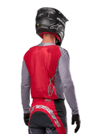 Pilote de motocross de dos portant le maillot Alpinestars 2024 Supertech Dade en Iron Red Berry et gris, doté d'un panneau arrière en mesh respirant et de logos argentés, associé à un casque noir et un pantalon de course assorti pour une performance tout-terrain professionnelle.