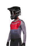 Alpinestars 2024 Supertech Dade Jersey, maillot de motocross, rouge et gris, à manches longues avec perforations découpées au laser, porté par un pilote avec casque et gants noirs, coupe de course athlétique professionnelle
