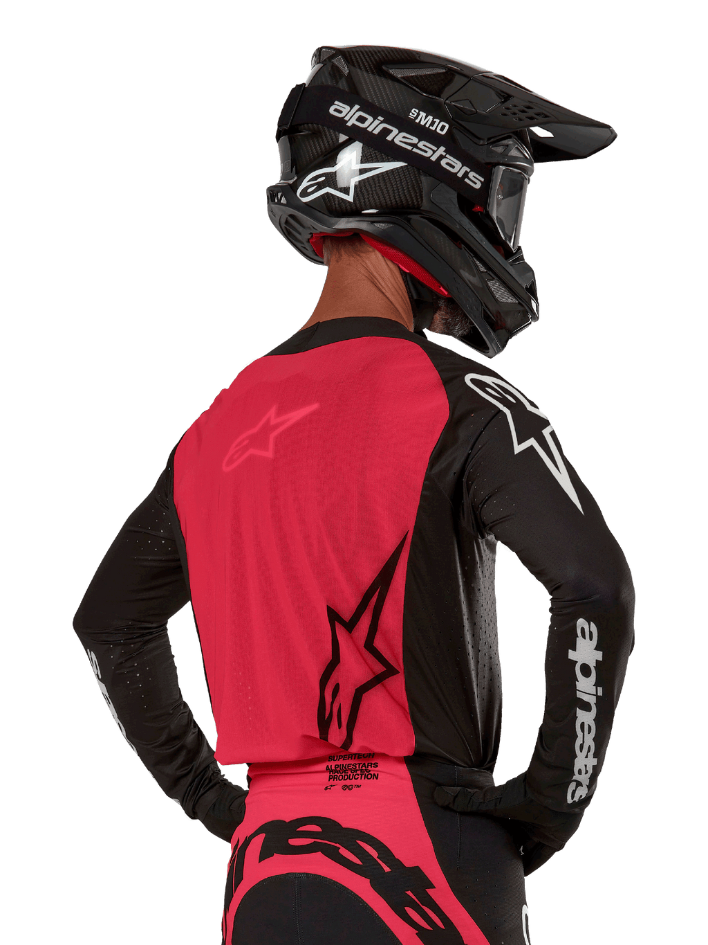Maillot Alpinestars Supertech Ward 2024, maillot de motocross, noir et rouge berry, vue arrière montrant le panneau en maille rouge et les manches noires avec logo blanc, porté avec un casque en fibre de carbone noir et des gants, coupe de course athlétique pour la conduite tout-terrain