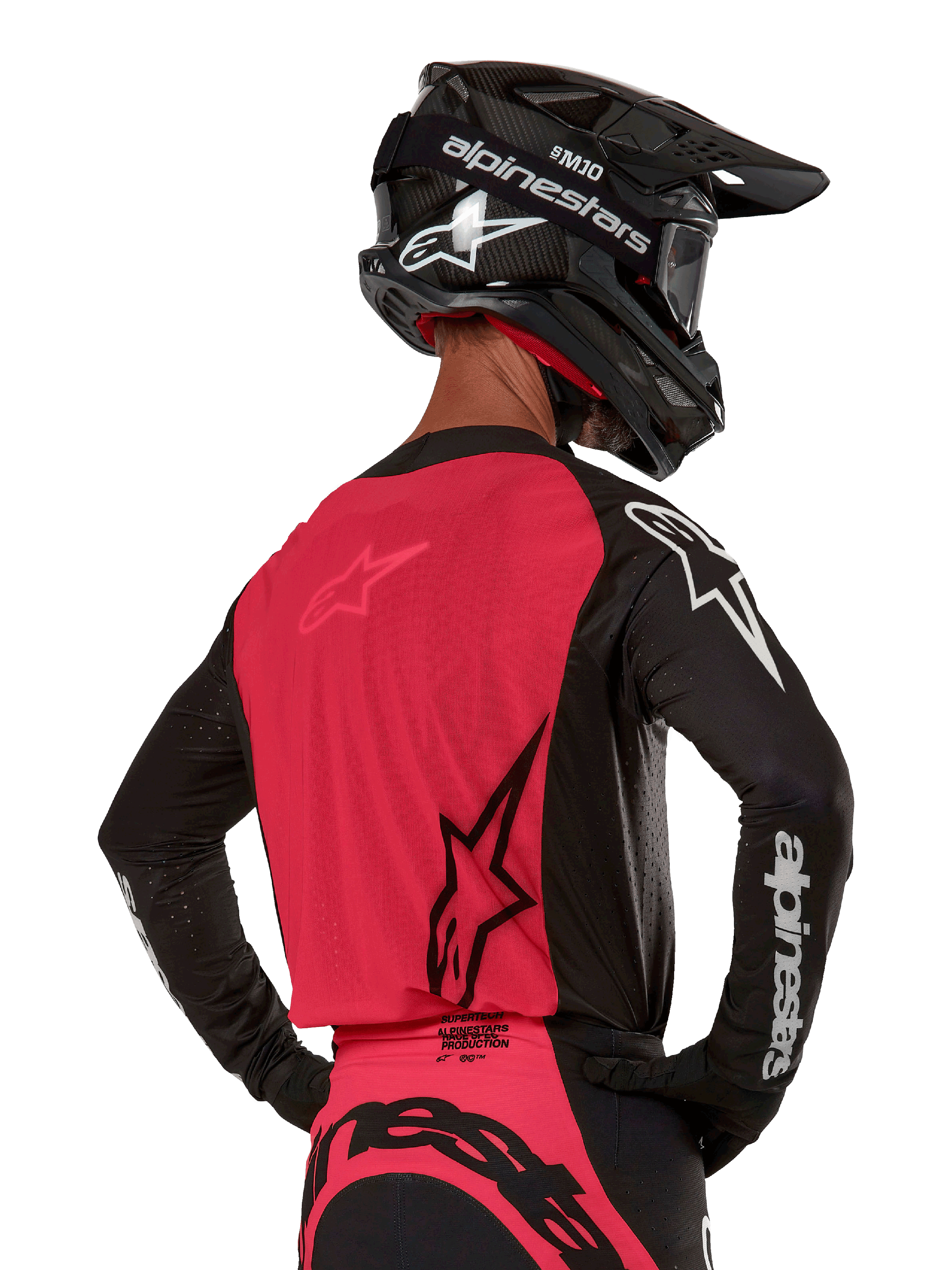 Maillot Alpinestars Supertech Ward 2024, maillot de motocross, noir et rouge berry, vue arrière montrant le panneau en maille rouge et les manches noires avec logo blanc, porté avec un casque en fibre de carbone noir et des gants, coupe de course athlétique pour la conduite tout-terrain