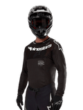 Maillot Alpinestars Supertech Ward 2024, maillot de motocross à manches longues, noir et blanc, équipement de performance avec logo Alpinestars audacieux, porté avec un casque et des gants assortis, coupe athlétique pour la conduite tout-terrain
