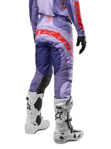 Alpinestars 2024 Techstar Ocuri Pants, pantalon de motocross, violet avec logos orange vif, vue arrière, accompagné de bottes blanches et gants noirs, équipement de protection technique pour le tout-terrain