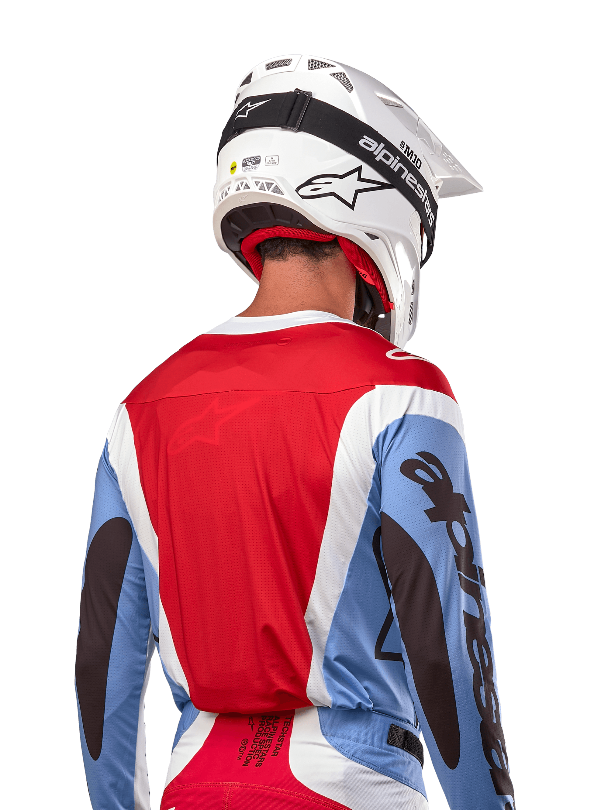Alpinestars Maillot Techstar Ocuri 2024, maillot de motocross, bleu clair, rouge Mars et blanc, vue arrière d'un pilote portant un casque blanc assorti et des lunettes noires, avec marquage noir audacieux sur les manches et coupe ergonomique pour la performance tout-terrain