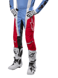 Alpinestars Techstar Ocuri Pants 2024, pantalon de motocross, bleu clair, rouge Mars et blanc, porté avec un maillot bleu clair et des bottes blanches, avec logo étoile sur la cuisse et genoux renforcés, équipement de course tout-terrain complet