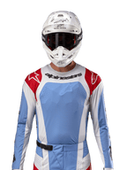 Maillot Alpinestars Techstar Ocuri 2024, maillot de motocross, bleu clair, rouge Mars et blanc, vue de face avec ventilation découpée au laser et coupe athlétique, porté avec un casque blanc et des lunettes pour un look de course tout-terrain professionnel