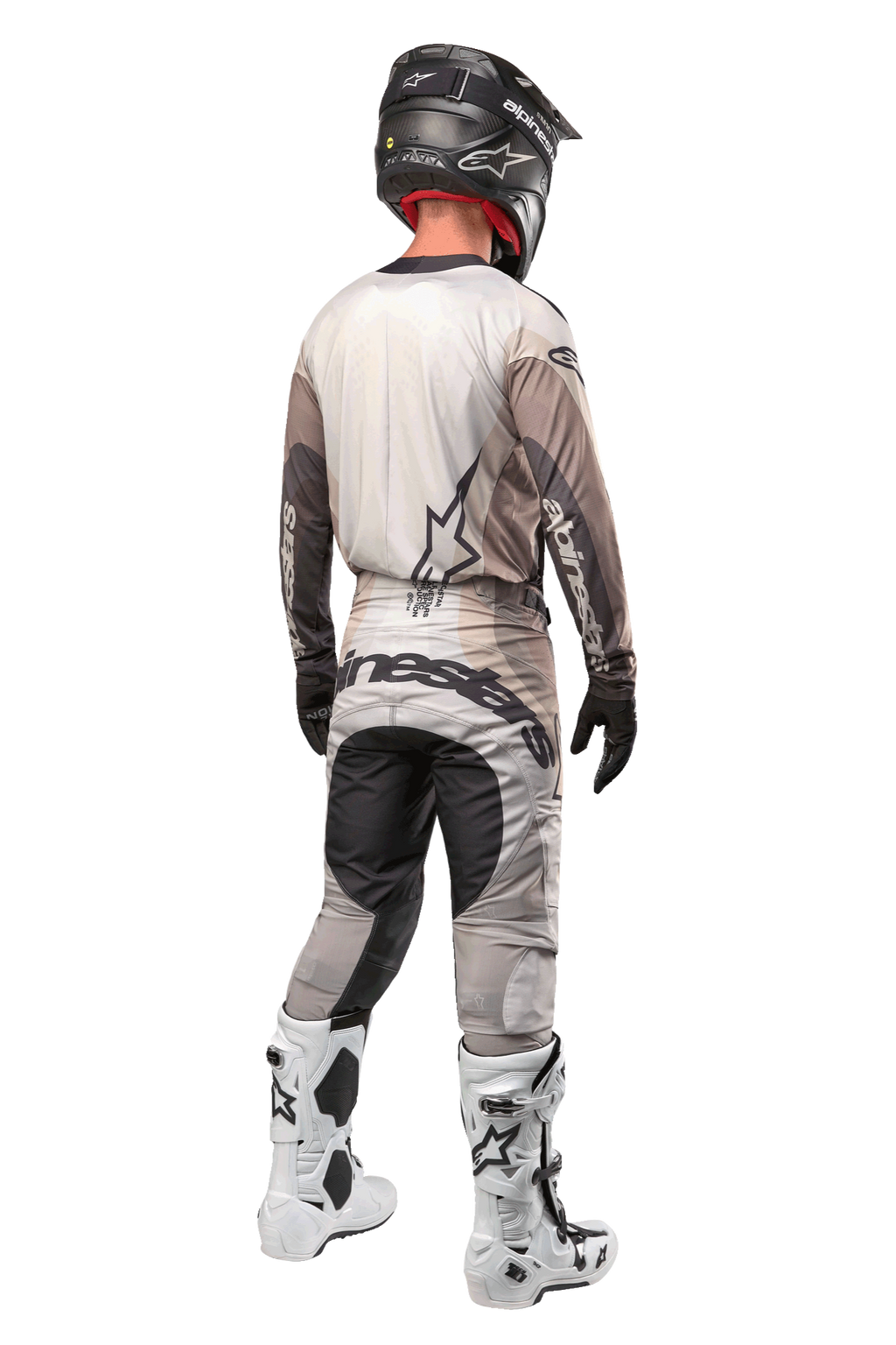 Alpinestars 2024 Techstar Pneuma Pants, pantalon de motocross, sable foncé et gris, vue arrière porté par un pilote avec un maillot assorti, des bottes blanches et noires et un casque noir, avec un marquage Alpinestars imposant sur l'assise et des panneaux sombres renforcés
