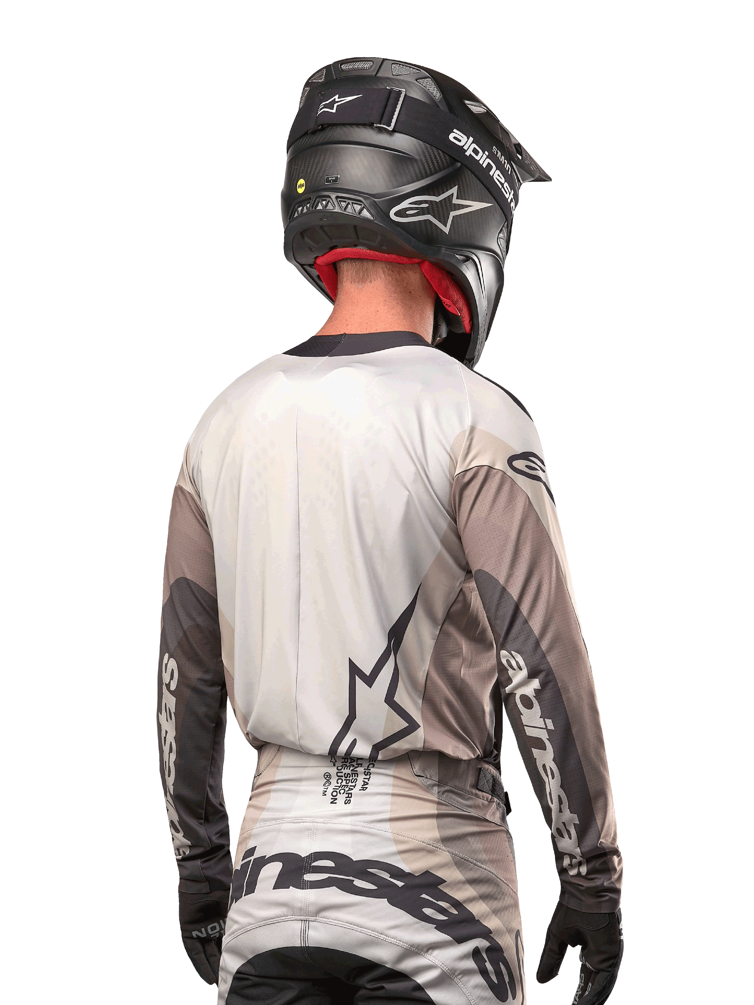 Pilote de motocross vu de dos portant le maillot Alpinestars 2024 Techstar Pneuma en Dark Sand Iron Dust Gray, associé à un casque noir à finition carbone, avec un grand logo étoile dans le dos et le marquage Alpinestars sur les manches.